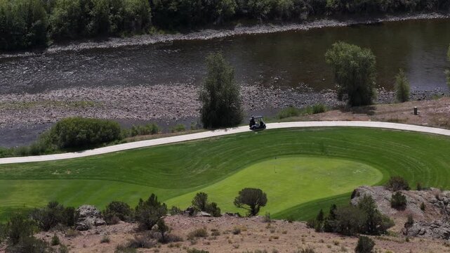 Aerial of golf course near Rio Grande river in South Fork Colorado in summer with manicured green fairways and golf cart on paved path
