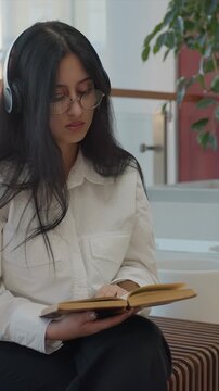 Close up of young woman with long dark hair wearing glasses. Woman is dressed in white button up shirt over black pants. Scene shows minimal movement as woman slightly turns her