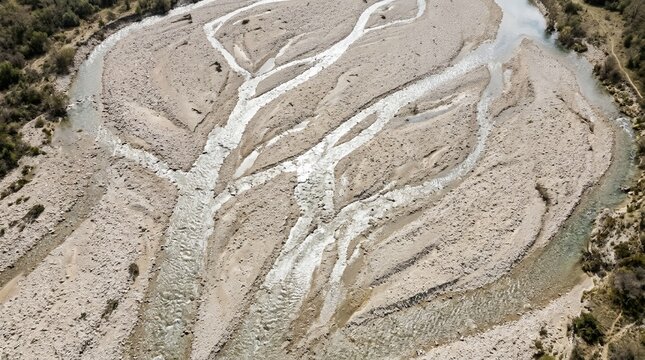 Aerial view of a braided river bed with intricate water patterns flowing through sand and gravel deposits in a valley