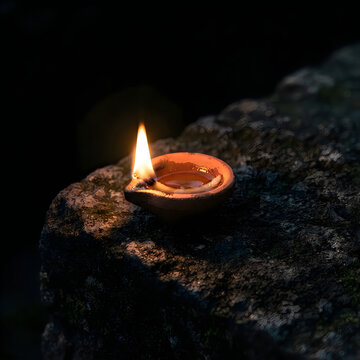 Small terracotta oil lamp burning with a bright flame on an ancient stone wall during dusk diya lamp traditional lighting flame glow ancient rock candlelight
