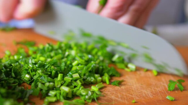 Green herb stems finely chopped by sharp knife on wooden board extreme close-up