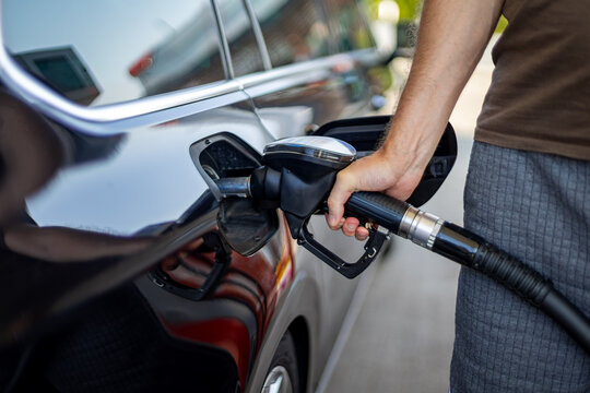 Person Refueling Black Car at Gas Station. Close-up of a person holding a fuel pump nozzle inserted into the open filler neck of a glossy black car at a gas station.
