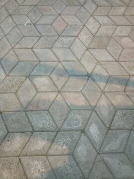 A high-angle shot of a grey, geometric concrete paver pathway with a subtle 3D cube pattern and soft diagonal shadows.