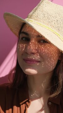Vertical video of young beautiful happy brunette woman in straw hat smiling on the pink background