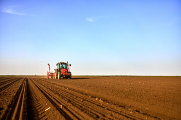 Naklejka premium Farmer in a red tractor seeding a large open field under a clear blue sky