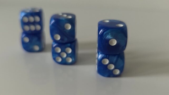 Close-up video of blue dice stacked in small vertical towers, viewed from different angles with shallow depth of field. Concept of balance, risk, probability, uncertainty, strategy and chance.
