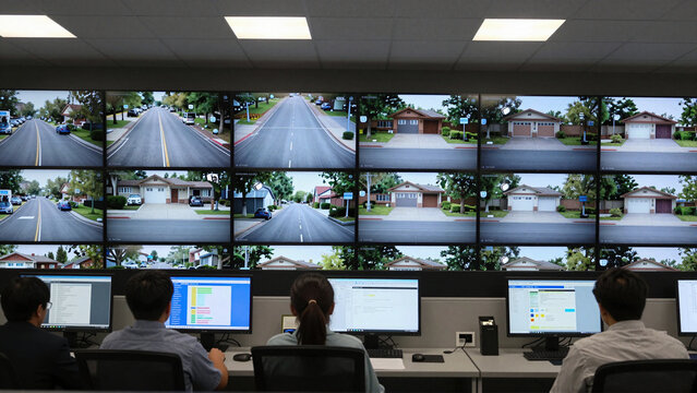 Security operators monitor suburban streets across surveillance screens in a modern control room