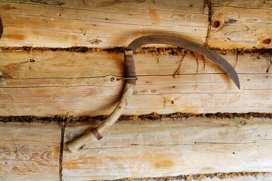 An antique metal sickle on the wall in a wooden hut. Household items, folk crafts. World tourism.