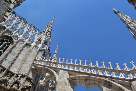 Dramatic low angle of milan duomo flying buttresses and pointed pinnacles against blue sky for architectural background and design composition