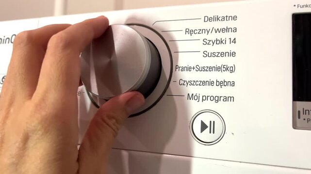 A hand turns the main program knob on a white washing machine control panel, home appliance services, technology, clean home.