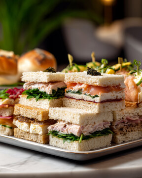 Assorted gourmet tea sandwiches served on a tray. Elegant catering food with salmon, tuna and fresh greens. Mini finger sandwiches for party buffet or high tea