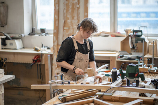 Talented woman crafter blue-collar worker engaged in work process at workbench in carpentry studio, craftswoman restoring wooden frame using mallet at worktable, handwork and creativity in restoration