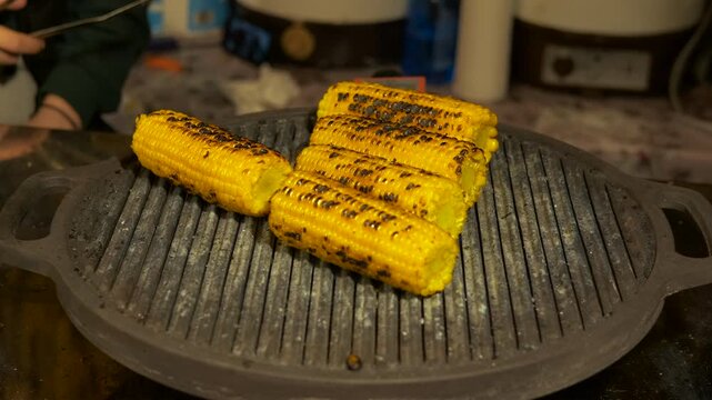 Delicious corn on the cob grilling on a hot plate. Fresh yellow sweet corn grilling on a hot cast iron plate, sizzling and smoking during the cooking process. A perfect healthy vegetarian meal