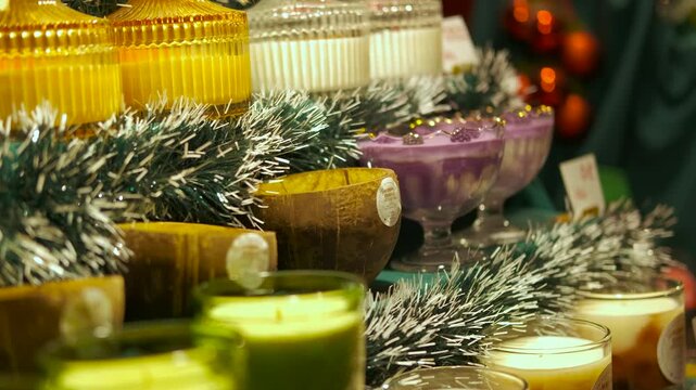 Colorful decorative scented candles christmas display. Variety of colorful handmade scented candles in decorative jars, displayed on a shelf with festive tinsel for sale at a christmas market