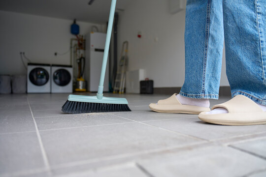 Woman sweeps dust and debris from tiled garage floor with a broom