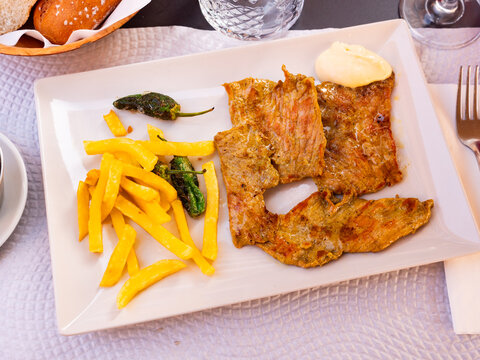 Fried pork pieces with potatoes and green peppers on a plate. Meat with vegetables for lunch