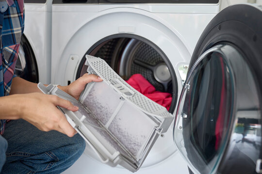 Woman holds dirty lint filter removed from an open tumble dryer. Concept of dryer maintenance