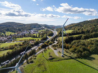 A wind turbine stands by a busy highway with cars moving along the road. The scene combines renewable energy with modern mobility. © 24K-Production