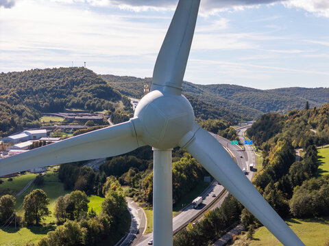Wind turbine stands tall next to a busy highway blending clean energy and modern transport during daylight hours