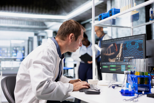 Chemist in a biolab studies experiment data on a computer with fascination and curiosity, reading unusual biotechnology research results and an intriguing scientific discovery in medical research.