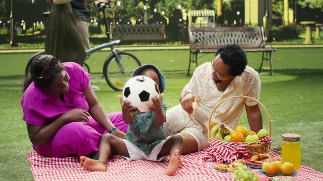 Playful boy playing catch and throwing ball at parents at picnic
