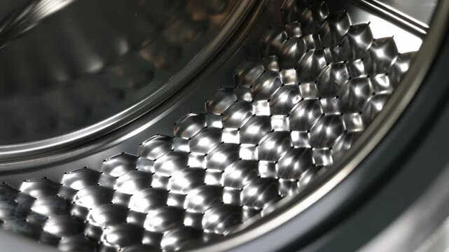 Stainless steel washing machine drum rotating. Empty stainless steel drum of a modern washing machine with a special honeycomb texture rotating slowly, showing a close-up of the polished metal