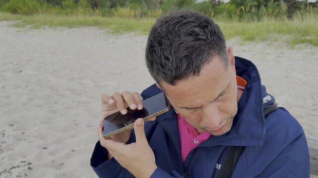 Close-up of a visually impaired adult man using a mobile phone or screen reader accessibility feature outdoors during the day. Stationary footage focusing on his face and hands. 