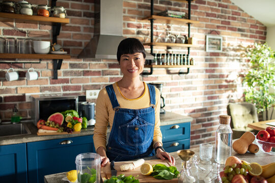 Smiling woman making healthy smoothie in home kitchen