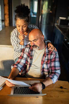Middle-aged couple reviewing finances on laptop at kitchen table
