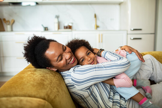 Smiling mother hugging daughter on sofa at home