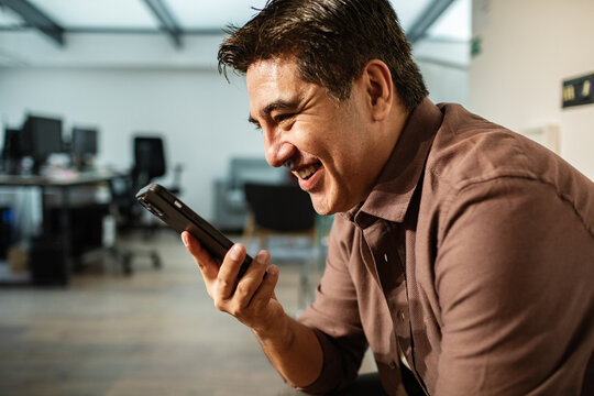 Smiling businessman recording voice message in modern office