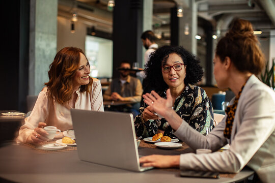 Three businesswomen collaborating with laptop in cafe