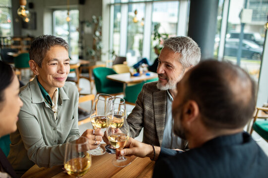 Mature friends toasting white wine at restaurant
