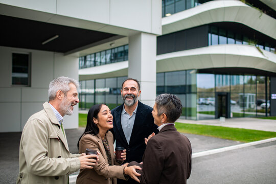 Business colleagues laughing during coffee break outside modern office