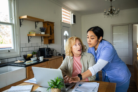 Home nurse helping senior woman with bills on a laptop in the kitchen