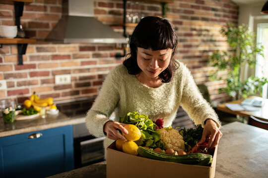 Woman unpacking organic produce box in home kitchen