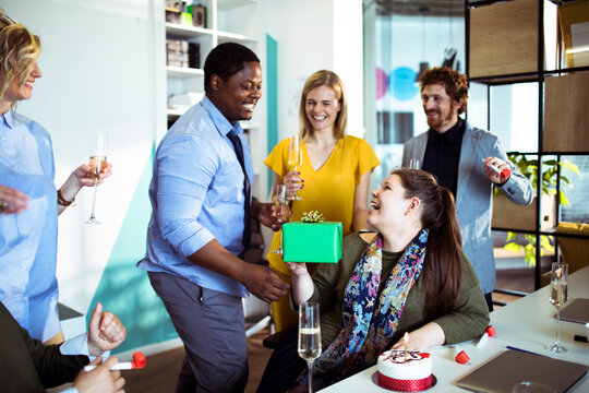 Coworkers celebrating a birthday with gift and cake in modern office
