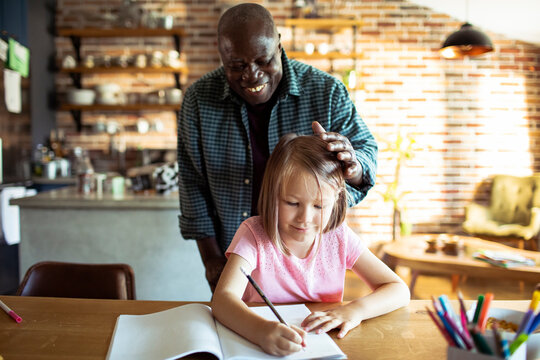 Smiling man helping girl with homework at home kitchen table