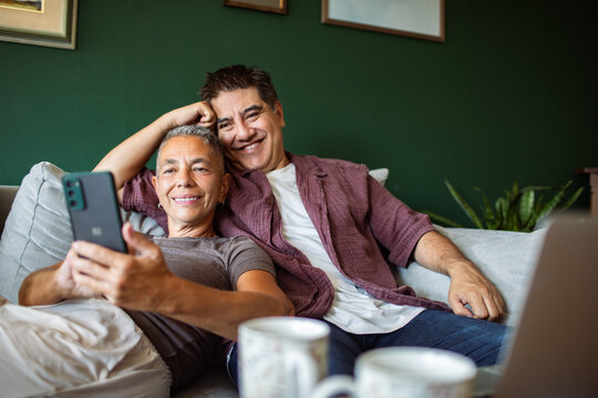 Mature couple relaxing at home on sofa, looking at smartphone
