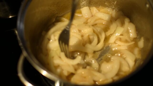 Onions stirring in a pot with a fork. 