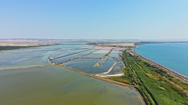 Salt pans are visible along the coastline with water on both sides. The landscape shows a clear sky and rows of salt fields. This view captures a rural setting.