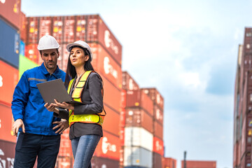 Worker with a tablet inspects rows of stacked shipping containers at a busy import export freight...