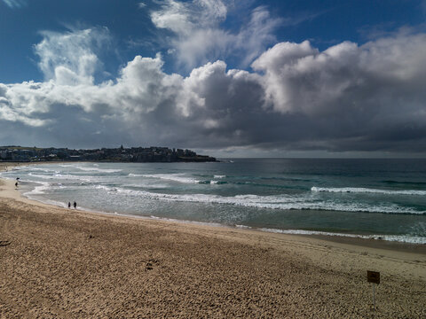 Bondi Beach, in Sydney with dramatic sky on a late winter sunny day. People walking on the sand.