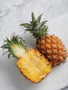 Two pineapples whole and halved on white speckled cutting board