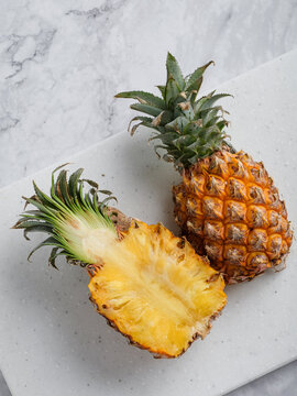 Two pineapples whole and halved on white speckled cutting board