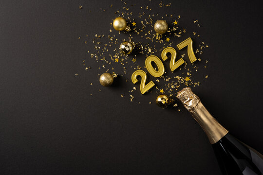 Happy New Year 2027 celebration with gold champagne, glitter numbers and festive ornaments on black banner background