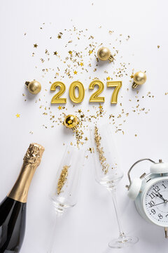 Happy New Year 2027 coming celebration with gold decorations champagne and confetti for winter holiday on vertical clean white tabletop