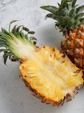 Two pineapples whole and halved on white speckled cutting board