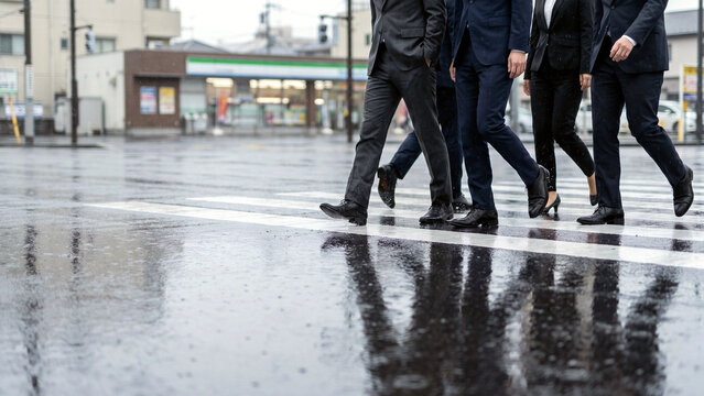 雨の横断歩道を濡れた路面の反射とともに渡るスーツ姿の一団