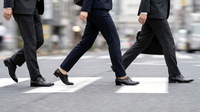 横断歩道を渡るスーツ姿のビジネスマン三人の脚元